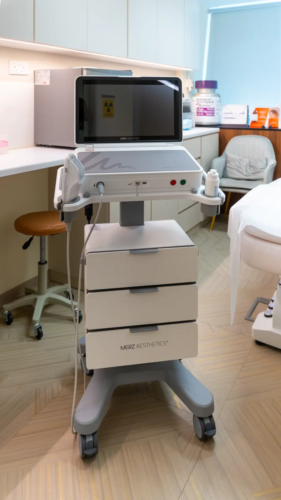 Ultherapy system with its screen raised, next to a treatment bed and chair