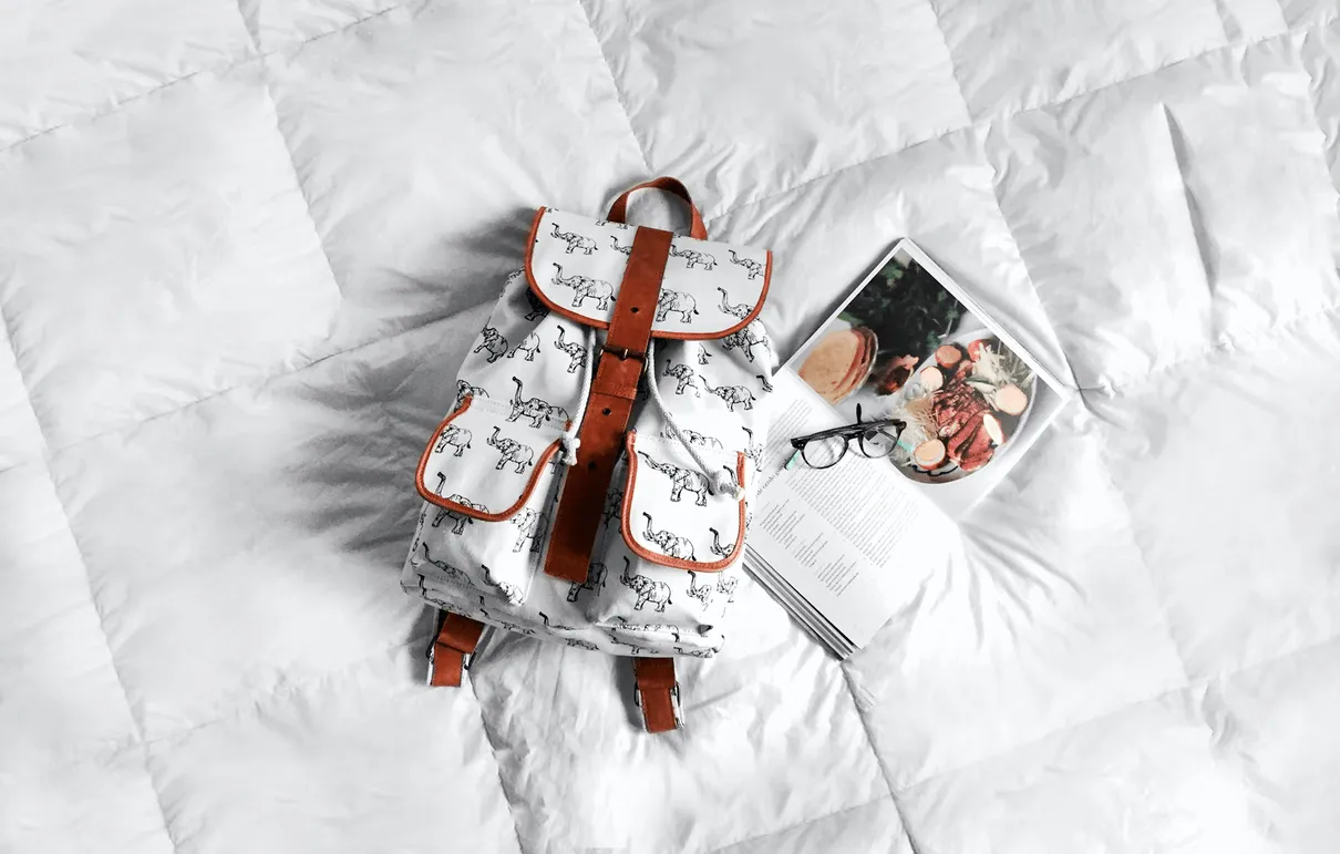 Travel bag and reading material laid out on a bed
